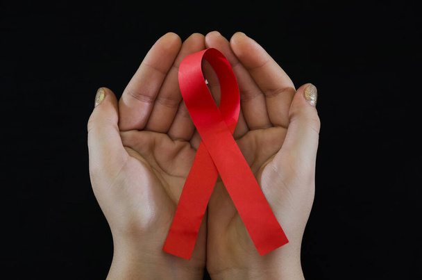 AIDS concept. Red ribbon in hands on black background  - Photo, image