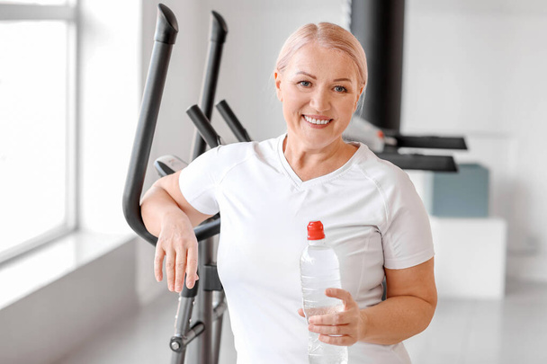 Deportiva mujer madura con botella de agua en gimnasio
 - Foto, imagen