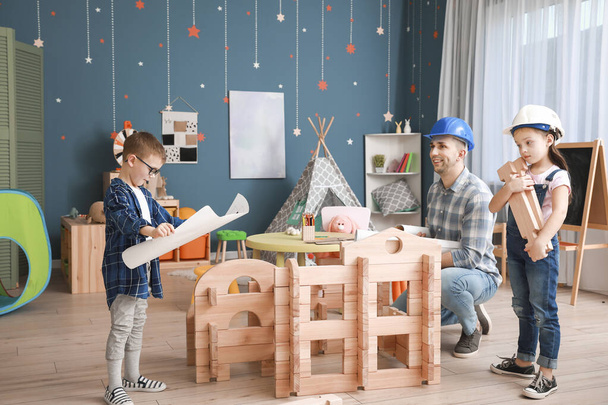 Padre e hijos pequeños vestidos como constructores jugando con casa para llevar en casa
 - Foto, Imagen