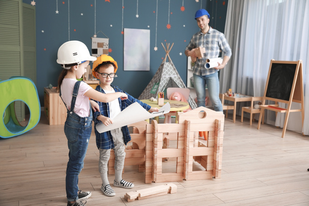 Père et petits enfants habillés en constructeurs jouant avec la maison à emporter à la maison
 - Photo, image