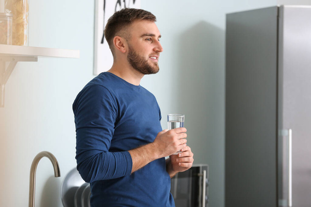 Молодой человек пьет воду на кухне
 - Фото, изображение