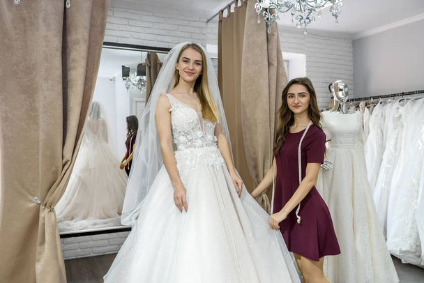 Saleswoman helping young bride in wedding salon - Valokuva, kuva