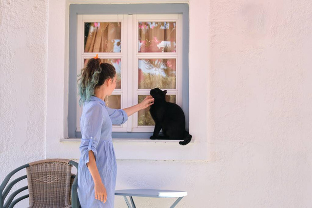 Teenager girl touching beautiful black cat sitting on the window sill outdoor - Zdjęcie, obraz