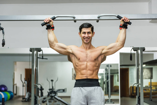 Sportive man making exercises on crossbar in gym - Photo, Image