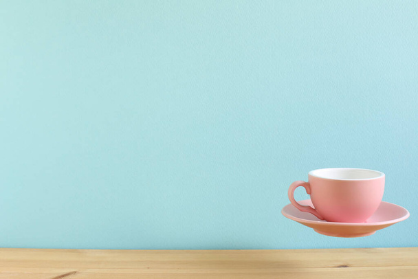 Růžový prázdný šálek kávy plovoucí na dřevěném stole. kopírovat prostor - Fotografie, Obrázek