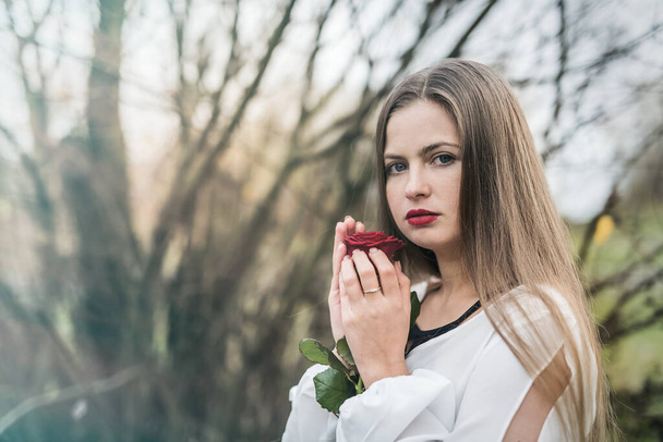 Krásná mladá žena s červenou růží pózující venku - Fotografie, Obrázek