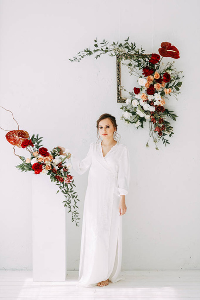 Red wedding decor of roses. Portrait of the bride in the style of fine art. Morning of the bride in the snow-white Studio.  - Фото, изображение