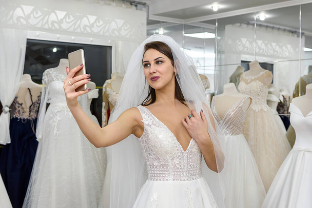 Mladá nevěsta dělá selfie ve svatebních šatech v salonu - Fotografie, Obrázek