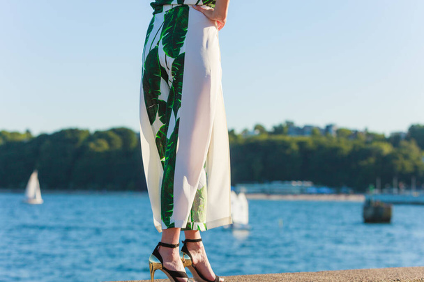 Woman legs wearing fashionable dress and high heels summer shoes. Female walking on sea coast. Yachts in the background - Φωτογραφία, εικόνα