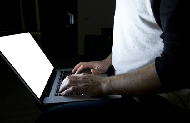 Młody człowiek siedzący wieczorem na kanapie z nowoczesnym laptopem i surfujący po sieci - Zdjęcie, obraz