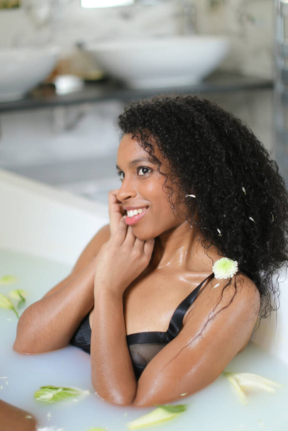 Relaxed nice black girl lying in milk bath and wearing swimsuit. - Photo, Image