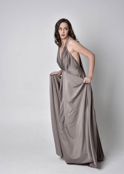 Portrait d'une jolie fille brune portant une longue robe de soirée argentée, pose debout sur fond de studio
 - Photo, image