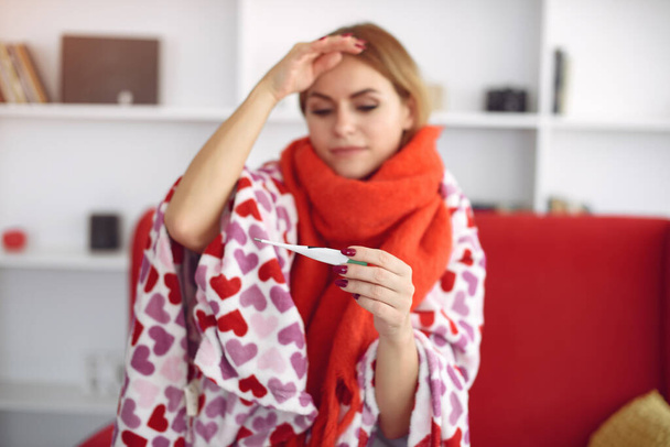 Woman sitting at home with a cold and measures the temperature - Foto, Bild