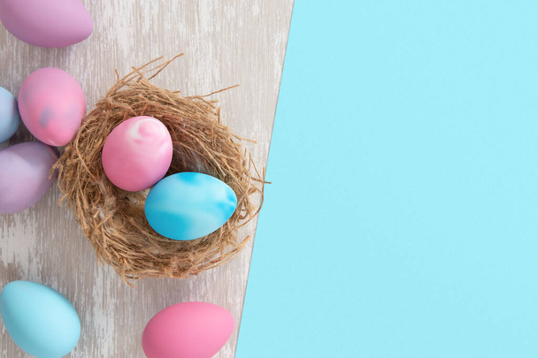 pastel pink and blue easter eggs in nest with blue paper split background for copy space - flat lay easter concept image - Photo, Image