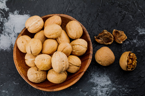 plate with some raw walnuts and peel on dark background. - Zdjęcie, obraz