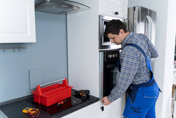 Male Technician In Overall Installing Oven In Kitchen - Foto, Imagem