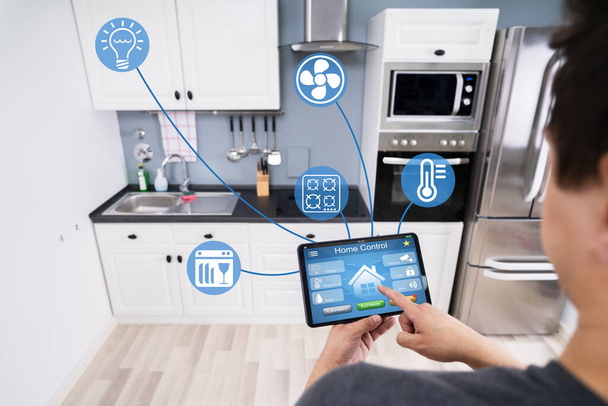 Primer plano de la mano de una persona usando la aplicación Smart Home en el teléfono inteligente en la cocina
 - Foto, imagen