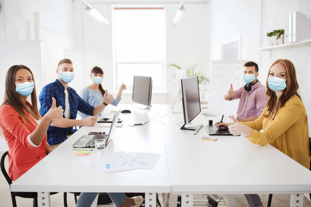 business team in medical masks showing thumbs up - Photo, Image