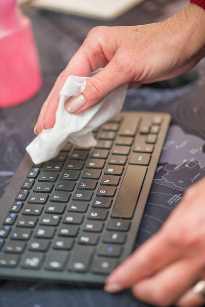 Женщина чистит компьютерную клавиатуру мягкой тканью. Коронавирусная профилактика и дезинфекция
. - Фото, изображение