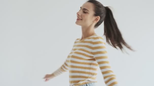 A happy satisfied young woman is whirling isolated over white background in studio - Footage, Video