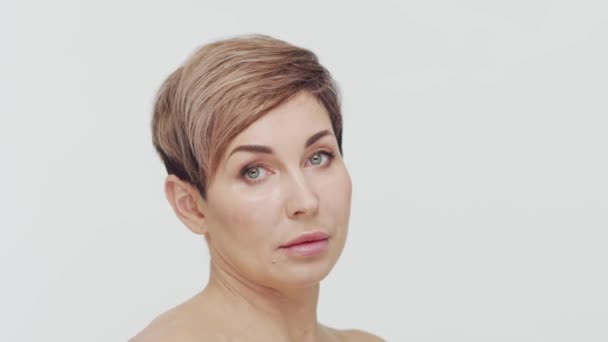 Close-up of middle aged mature woman over white bacjground. Portrait of mature lady. Plastic surgery, beauty injections, cosmetology concept. - Footage, Video