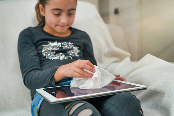 Nuori tyttö puhdistaa tabletin näytön pehmeällä liinalla. Coronavirus ehkäisy ja kodin desinfiointi. - Valokuva, kuva