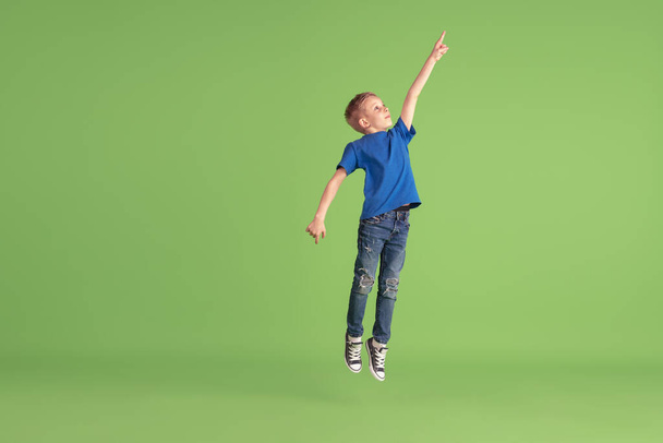 Happy boy playing and having fun on green studio background, emotions - Foto, imagen