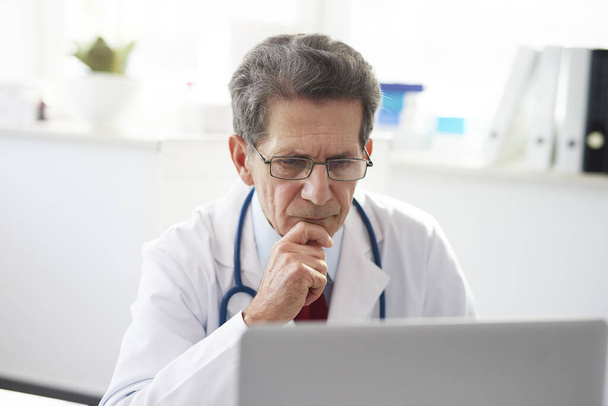 Senior arts werkt met een laptop in het kantoor van de dokter  - Foto, afbeelding
