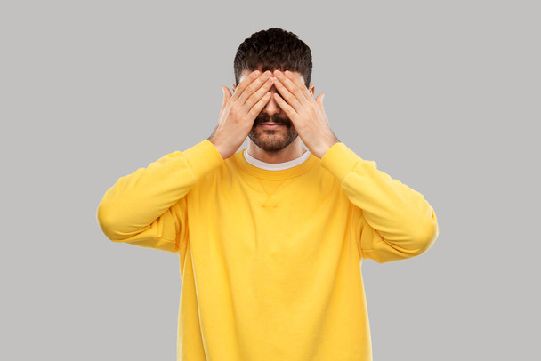 man in yellow sweatshirt closing his eyes by hands - Foto, Imagen
