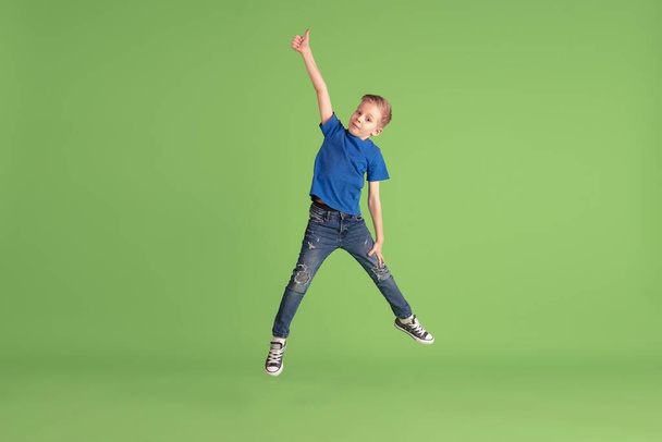 Happy boy playing and having fun on green studio background, emotions - Фото, зображення