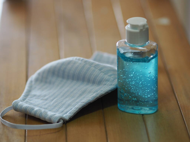 gel πλυσίματος στο χέρι σε πλαστικό μπουκάλι, ύφασμα Blue Mask σε φόντο ξύλο γραφείου σκόνη και μικρόβια pm 2.5, ιός covid 19, uv - Φωτογραφία, εικόνα
