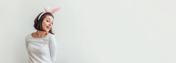 Frohe Ostern Feiertag Feder Konzept. Junge Frau mit Hasenohren auf weißem Hintergrund. Vorbereitung auf den Urlaub. Mädchen sehen glücklich und aufgeregt aus und haben Spaß am Ostertag. Banner - Foto, Bild