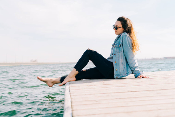 молодая красивая стильная девушка сидит на пирсе у озера
 - Фото, изображение