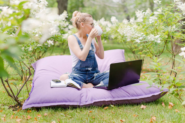 庭で働いているフリーランス。執筆、インターネットでサーフィン。公園エリアでリラックスして楽しんでいる若い女性。距離教育、フリーランスの概念. - 写真・画像