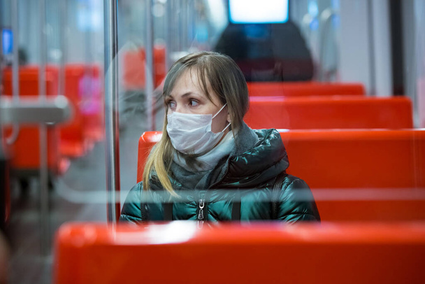 Woman in winter coat with protective mask on face sitting in subway car, using phone, looking worried. Preventive measures in public places of epidemic regions. Finland, Espoo - Foto, Bild