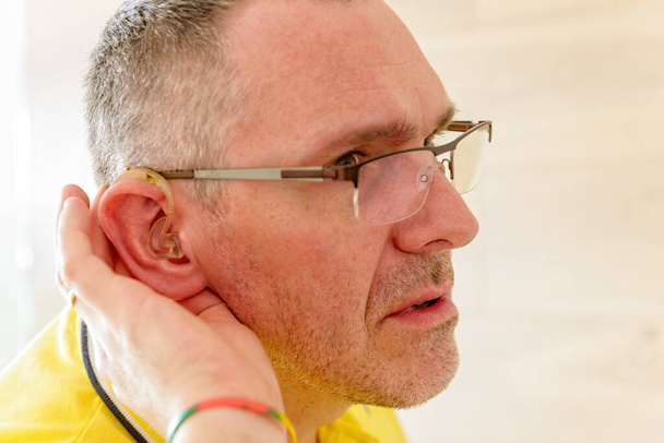 Man wearing deaf aid in ear attempting to hear something - Photo, Image