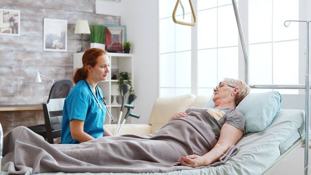 老人ホームで老人と病院のベッドで話している看護師 - 写真・画像