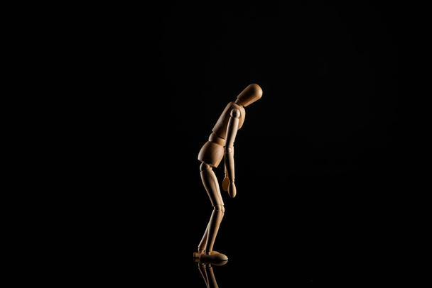 Wooden doll in leaning position on black background - Фото, изображение