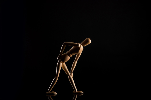 Wooden doll imitating touching knee on black background - Zdjęcie, obraz
