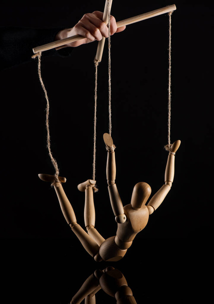 Cropped view of puppeteer holding wooden doll with ropes on black background - Foto, imagen