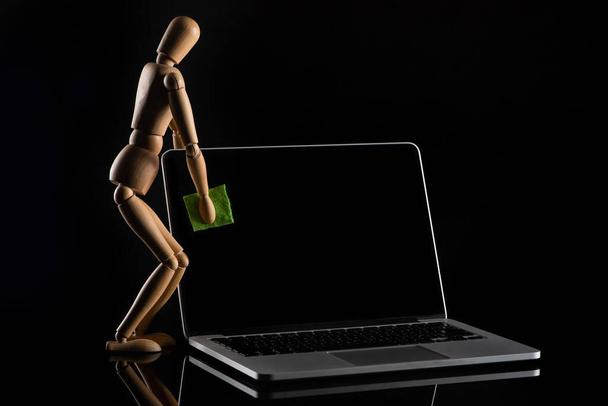 Ξύλινη κούκλα που μιμείται ξεσκονίζει φορητό υπολογιστή σε μαύρο  - Φωτογραφία, εικόνα