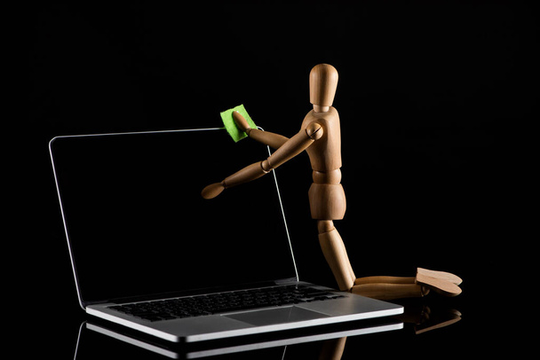 Wooden doll on knees position imitating dusting laptop on black  - 写真・画像