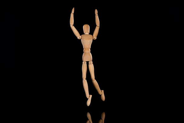 Wooden doll imitating dancing with outstretched hands on black  - Fotó, kép