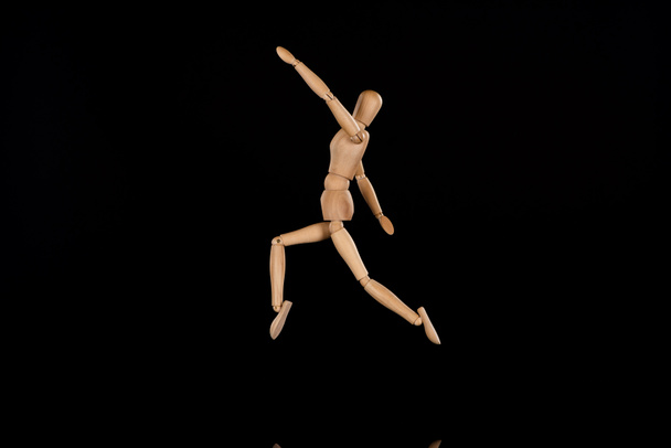 Wooden puppet imitating jumping on black background - 写真・画像