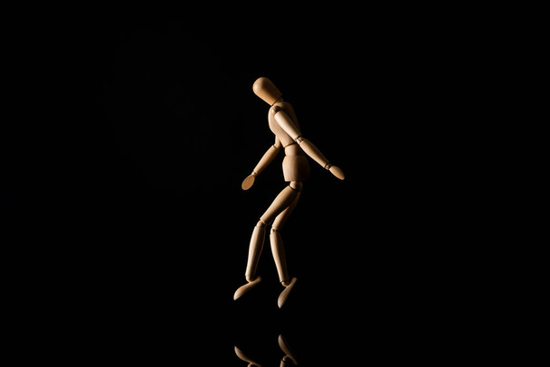 Wooden doll imitating tip toeing on black background - Foto, Imagem
