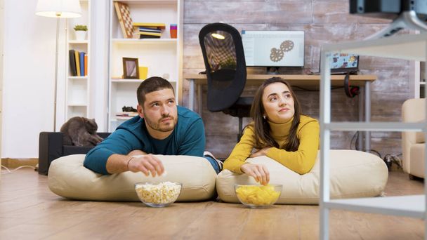 Χαρούμενο ζευγάρι που βλέπει τηλεόραση να κάθεται σε μαξιλάρια - Φωτογραφία, εικόνα