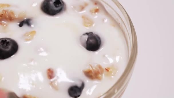 A woman mixes the ingredients in yogurt, granola, honey and berries. Healthy Dessert on white background, isolated macro shot - Footage, Video