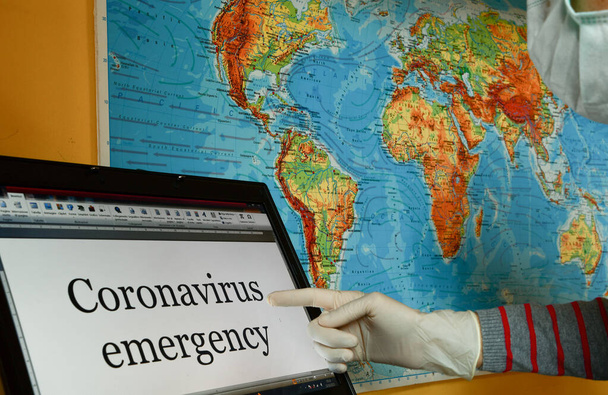 Dziewczyna ubrana w lateksowe rękawiczki i maskę chirurgiczną wskazującą na laptopa awaryjne Coronavirus słowa ze światem geograficznym jako tło - Zdjęcie, obraz