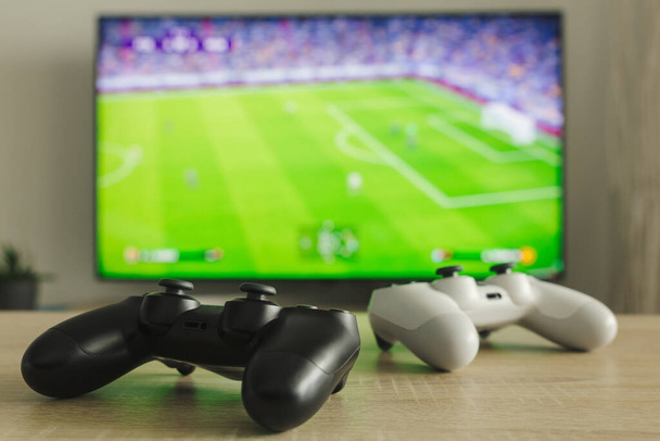 Stock photo of two gamepads on a table and a football game on TV in the background - 写真・画像