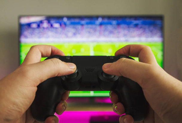 Στοκ φωτογραφία μερικών χεριών με ένα gamepad που παίζει ένα παιχνίδι ποδοσφαίρου στην κονσόλα παιχνιδιών - Φωτογραφία, εικόνα